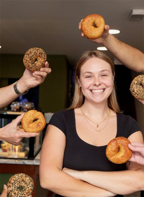 Emma, founder of The Bagel Box, surrounded by hands holding bagels